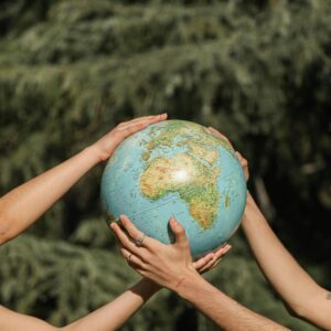 Four hands holding a globe outdoors, symbolizing unity and environmental conservation.